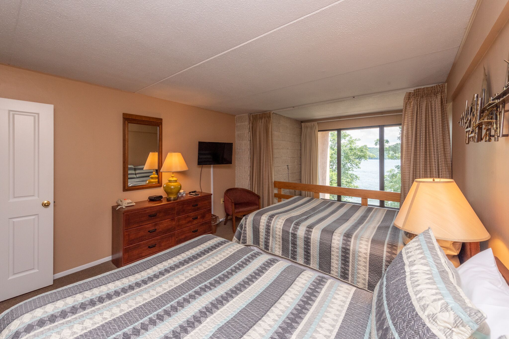 A hotel room with two beds, a wooden dresser, a TV, and a window with curtains.