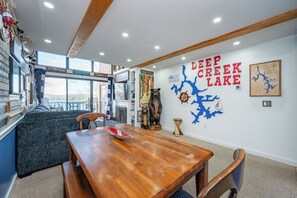 A dining area with a wooden table and chairs, a view of the lake, and a wall with a map and text.