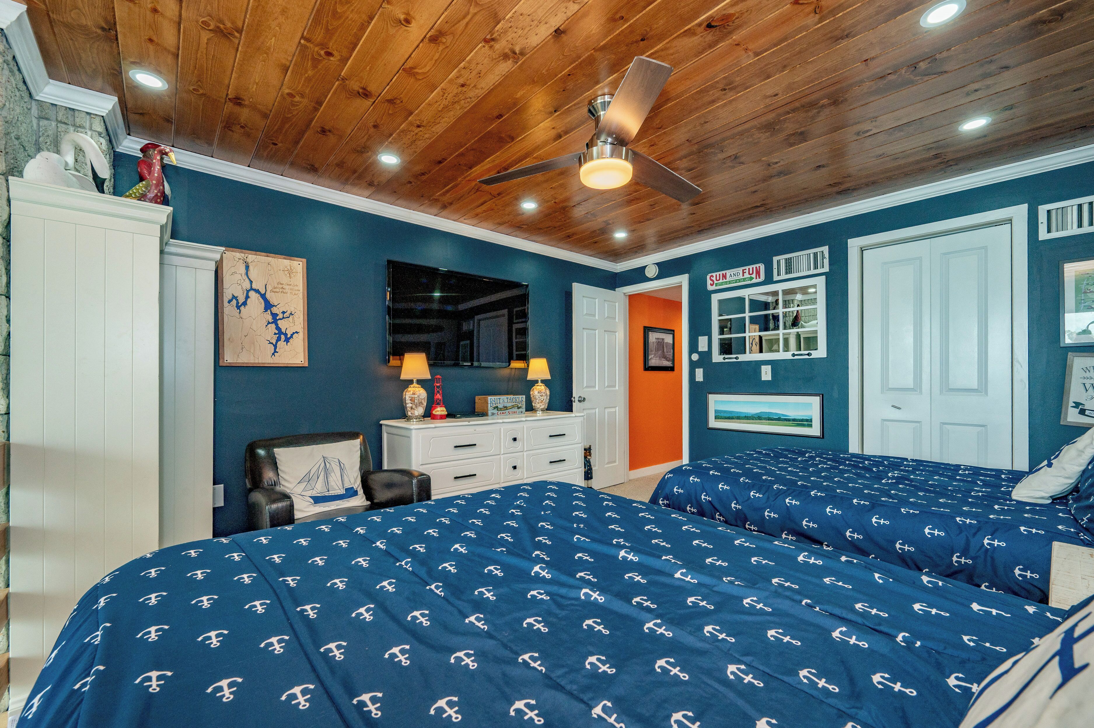 A bedroom with two beds, a ceiling fan, a dresser, and a door leading to another room.