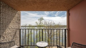 Un balcon agrémenté de meubles en osier, une petite table ronde et une vue sur un lac bordé d’arbres, sous un ciel dégagé.