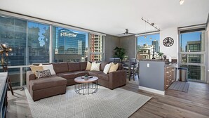 Ein modernes Wohnzimmer mit einem großen braunen Ecksofa, einem runden Couchtisch und einem Essbereich mit einer kleinen Kochinsel.