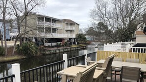 A waterfront patio with outdoor seating, a view of a river, and a multi-story building in the background. - Waterfront, Large deck, Pet friendly, Golf cart, Screened in porch. (Myrtle Beach)