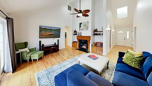 A spacious living room with a fireplace, a television mounted on the wall, and a ceiling fan. - Indoor Heated Pool & Hot Tub, Game room, EV Charger, Pets Welcome! (Bend)
