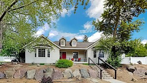 A two-story house with a red front door, a covered porch, and a stone retaining wall in front. - Indoor Heated Pool & Hot Tub, Game room, EV Charger, Pets Welcome! (Bend)