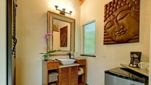Une salle de bain avec un meuble-lavabo en bois, un grand miroir, une statue de Bouddha, une machine à café et un lave-vaisselle.