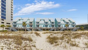 A beachfront hotel with multiple-story buildings, a sandy beach in front, and a clear sky. - 🏖️ Beachfront Family Fun – Pool, Switch & Karaoke (Gulf Shores)