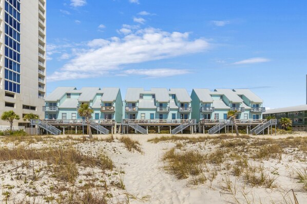 A beachfront hotel with multiple-story buildings, a sandy beach in front, and a clear sky.