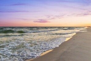 A beach with waves at the shore and a sunset in the background.