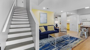 A modern apartment with a staircase, a living area with a blue sofa, a kitchen with white cabinets, and a patterned rug. - 🏖️ Beachfront Family Fun – Pool, Switch & Karaoke (Gulf Shores)