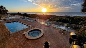 Ein Poolbereich auf dem Dach mit Whirlpool, Liegestühlen und Blick auf den Sonnenuntergang über dem Meer.