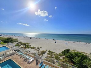 Ein Strand mit Poolbereich, Liegestühlen und blauem Himmel.