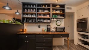 A kitchen with a wooden countertop, black cabinets, and a built-in shelf unit with various kitchen items. - Little Gem - Thoughtfully Curated Desert Escape (Tucson)