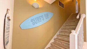 Una escalera con un letrero con forma de tabla de surf que dice "SURFS UP" en la pared.