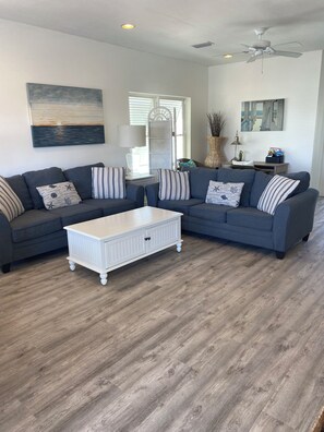 A living room with a grey sectional sofa, a white coffee table, and a ceiling fan. - BEACH HOUSE including 100 DOLLAR GC with a 4 day or more STAY. (Pensacola Beach)