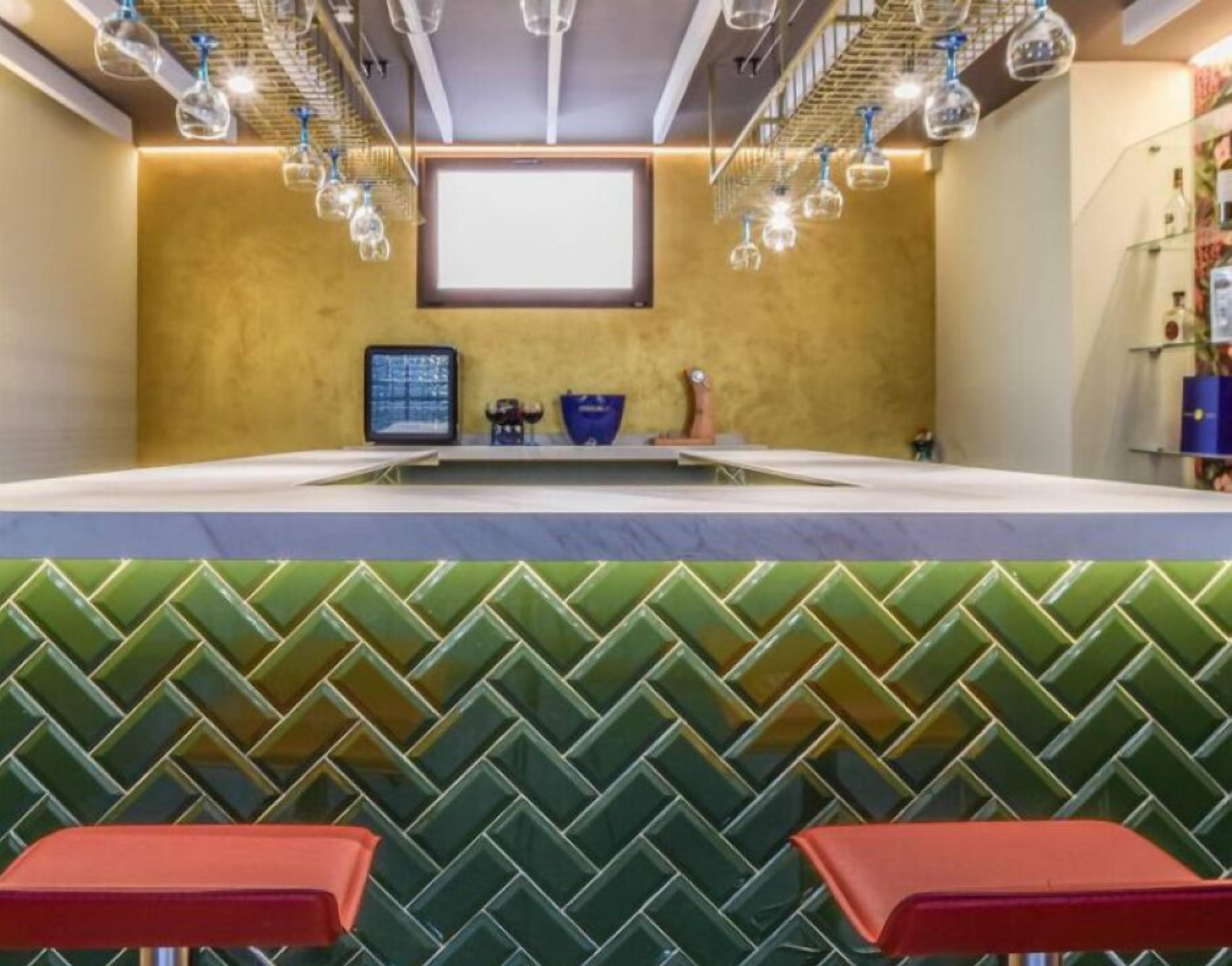 Un espace bar avec un mur à motifs verts, un grand écran et des luminaires suspendus.