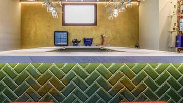 Un espace bar avec un mur à motifs verts, un grand écran et des luminaires suspendus.