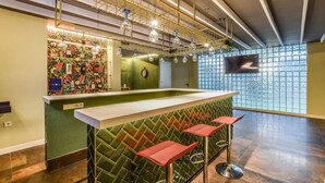 A bar area with a green patterned wall, a white counter, and red bar stools.
