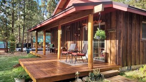 A wooden cabin with a porch, outdoor seating, and a view of the surrounding forest. - Couples Retreat, hot tub, private! (La Pine)