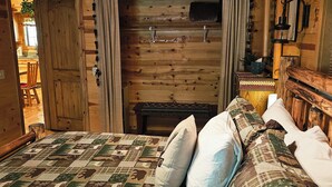 A wooden cabin interior with a bed featuring a quilt with animal prints, a wooden ceiling, and a rustic decor. - Couples Retreat, hot tub, private! (La Pine)