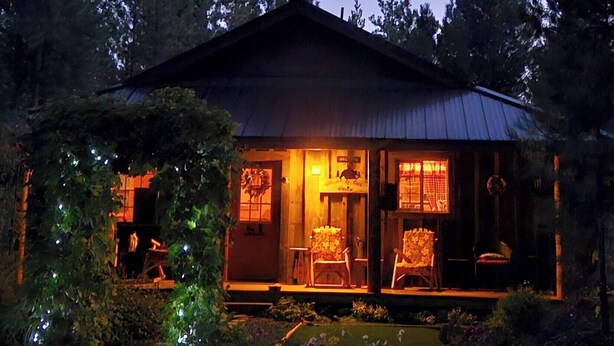 A wooden cabin with a porch, surrounded by trees and a garden. - Couples Retreat, hot tub, private! (La Pine)