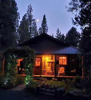 A wooden cabin with a porch, surrounded by trees and a garden.