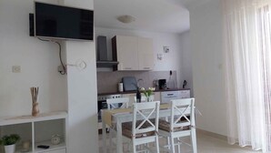 Una cuina compacta amb armaris blancs, un forn integrat i zona de dinar amb caires blancs.