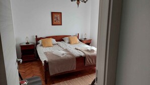 Un llit ben fet amb un capçal de fusta, dues taules de nit amb làmpades, una fotografia emmarcada a la paret i un sòl de fusta.