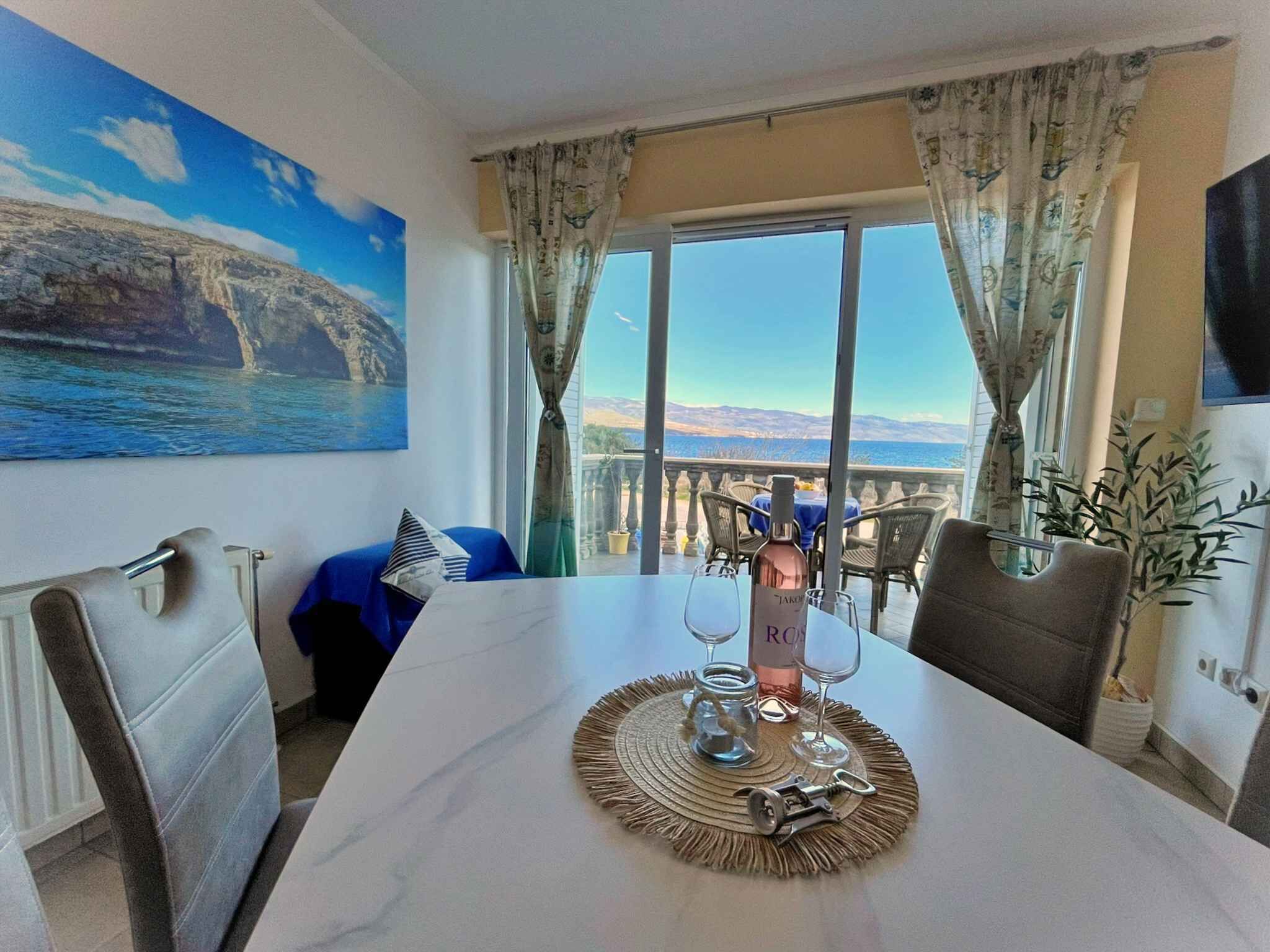 Uma sala de jantar com mesa posta para dois, uma garrafa de vinho e uma vista panorâmica através de grandes janelas.
