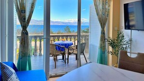 Ein Zimmer mit Bett, Fernseher, einem Balkon mit Tisch und Stühlen sowie Meerblick.