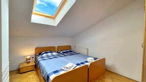 Ein kleiner, heller Raum mit Oberlicht, einem Bett mit karierter Bettwäsche, einem Nachttisch mit Lampe und einer Heizung.