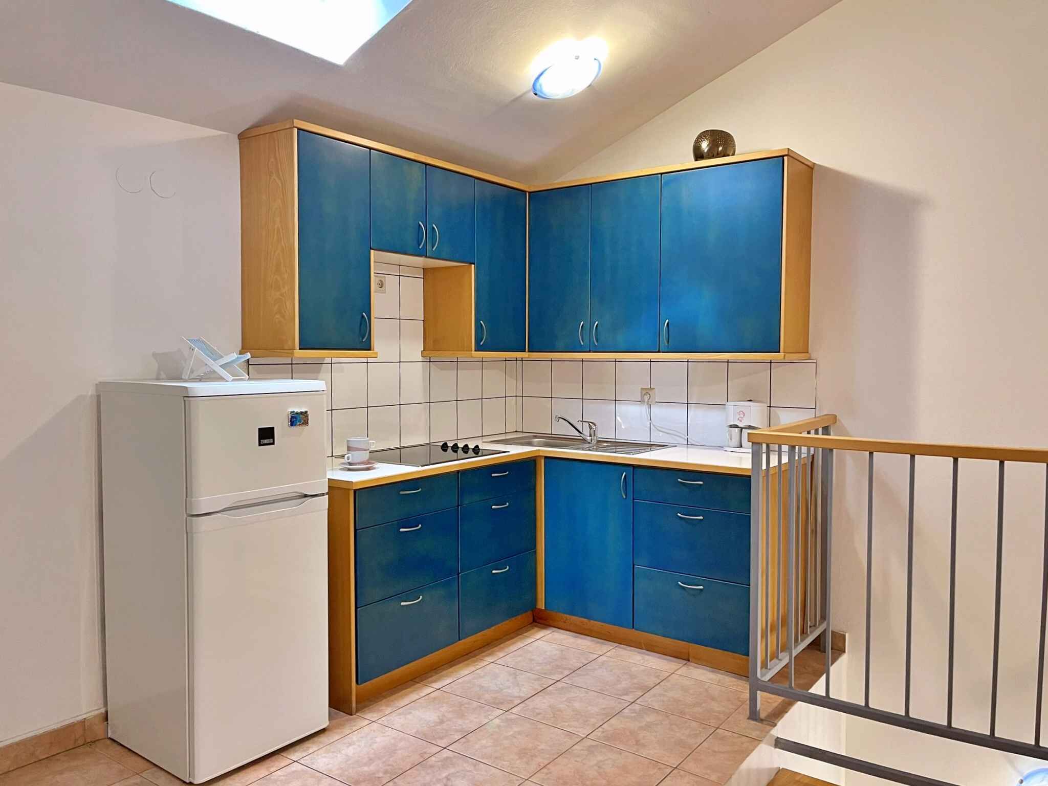 Een kleine keuken met blauwe kastjes, een witte koelkast en een gasfornuis.