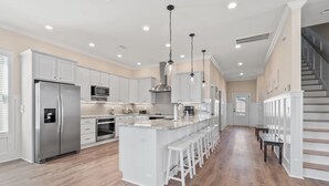 A spacious kitchen with white cabinetry, stainless steel appliances, and a central island with bar stools. - Modern Luxury Home w/ Private Pool - Cherry Grove Beach (North Myrtle Beach)