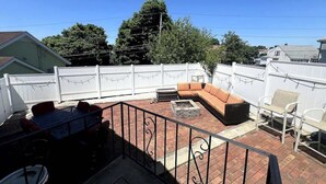 A backyard patio with a brick floor, a fire pit, a sofa, and a dining table. - Stylish 3BR Home Close to Campus 10min to Boston (Everett)
