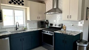 A modern kitchen with dark blue cabinets, a stainless steel range hood, a built-in oven, and a dishwasher. - Stylish 3BR Home Close to Campus 10min to Boston (Everett)