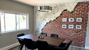 A dining area with a brick wall, a wooden table, and black chairs. - Stylish 3BR Home Close to Campus 10min to Boston (Everett)