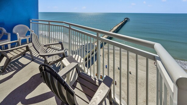 A balcony with chairs overlooking a beach and a pier.