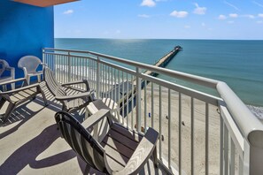 Un balcon avec des chaises donnant sur une plage et une jetée.