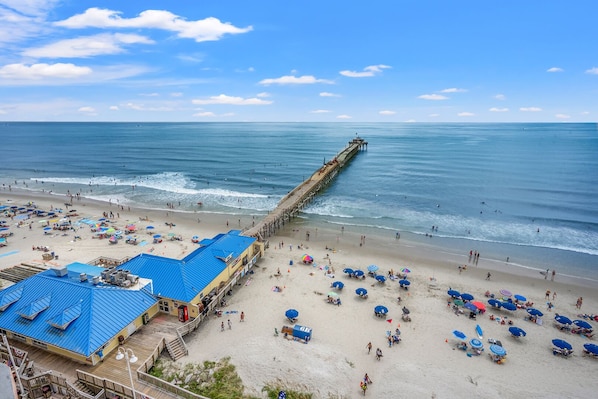 A beach with a pier extending into the ocean, umbrellas, and beach chairs.
