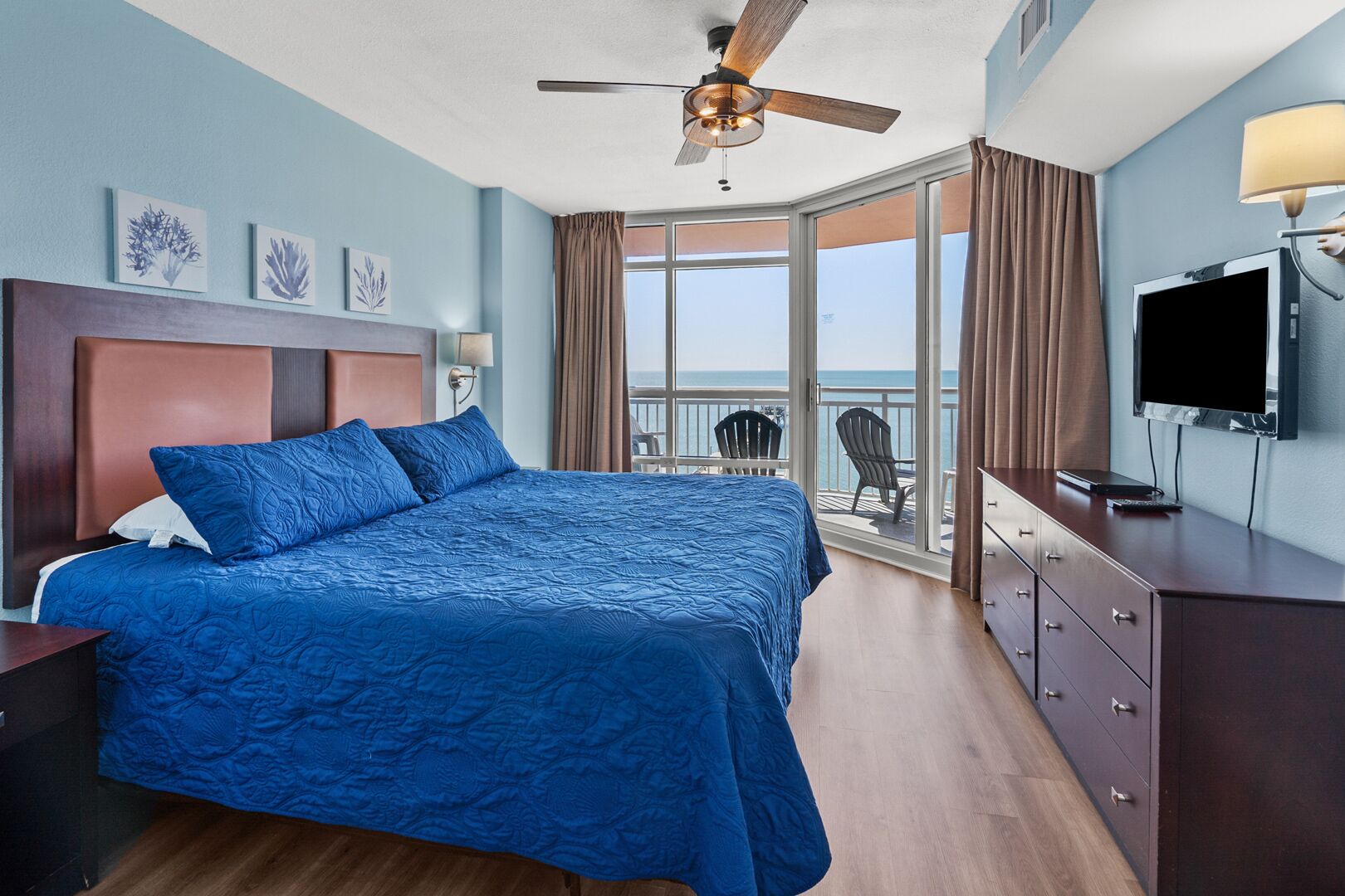 Une chambre d’hôtel avec un grand lit, un ventilateur de plafond, une télévision et un balcon offrant une vue sur l’océan.