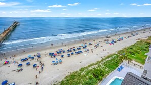 A beach with umbrellas and lounge chairs, a pier, and a pool.