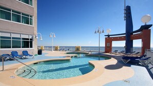 A pool area with lounge chairs and a view of the ocean.