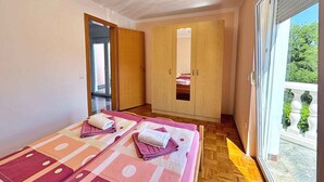 Une chambre avec deux lits, une armoire en bois et une porte-fenêtre coulissante donnant sur un balcon.