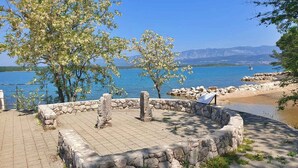 Une zone dallée de pierres, avec un mur de pierres, des arbres et une vue sur un lac et des montagnes.