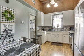 Una cocina con armarios blancos, mantel a cuadros y una corona colgante.