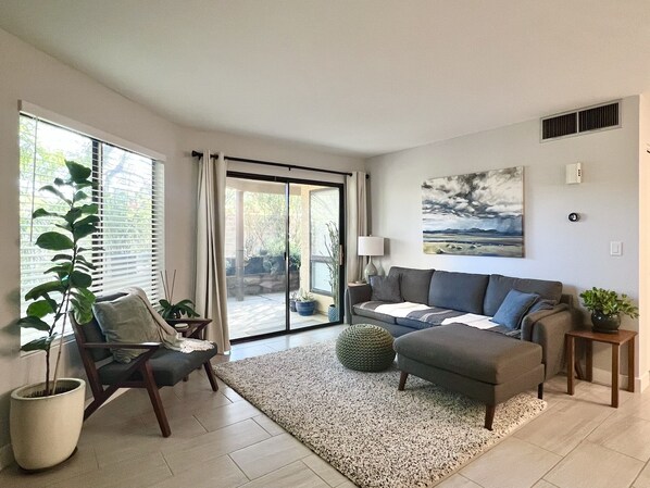 A modern living room with a sofa, armchair, and a large window with blinds.