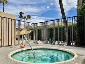 A swimming pool with a metal fence, surrounded by palm trees and a building.