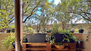A wooden bench with potted plants in an outdoor area with a stone floor and a view of trees and sky. - Contemporary Condo with Private Garden Patio and Pool Access (Tucson)