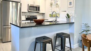 A modern kitchen with white cabinets, stainless steel appliances, a large island with stools, and artwork on the walls. - Contemporary Condo with Private Garden Patio and Pool Access (Tucson)