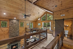 A wooden cabin interior with a stone fireplace, wooden ceiling, and large windows.