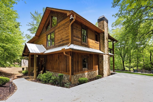 A two-story log cabin with a stone chimney, large windows, and a covered porch.